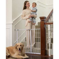 a woman holding a baby in her arms while standing next to a dog on the floor