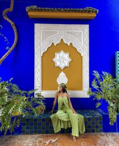 a woman is sitting on a bench in front of a blue wall and potted plants