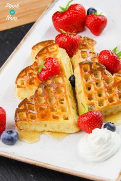 two waffles with strawberries and whipped cream on a white plate next to berries