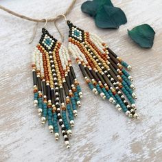 a pair of beaded earrings on top of a wooden table next to green leaves