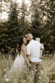 a man and woman holding a baby standing in tall grass with trees in the background