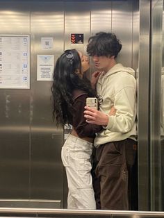 a man and woman standing next to each other in front of a metal elevator door