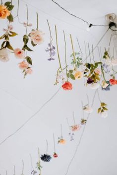 an arrangement of flowers hanging from the side of a white wall with string attached to it