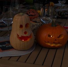 two carved pumpkins sitting on top of a table next to wine glasses and candles