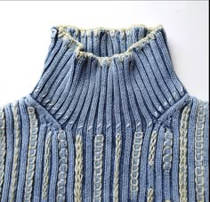 a close up of a blue and white sweater with chains on the collar, made from yarn