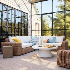 an outdoor living room with wicker furniture and large glass windows on the outside wall