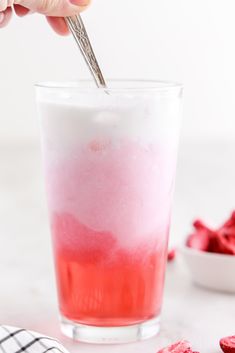 a hand holding a spoon over a red and white drink