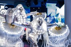 two women dressed in white dance with lights on their body and hands behind her back