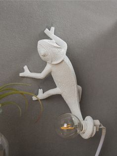 a white lizard figurine on the wall next to a light bulb