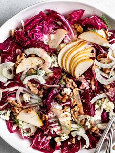 a white bowl filled with red cabbage, apples and walnuts next to a fork