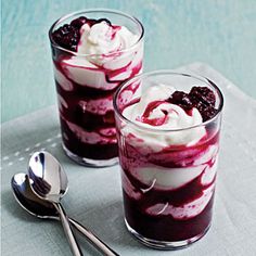 two glasses filled with dessert sitting on top of a white cloth next to spoons