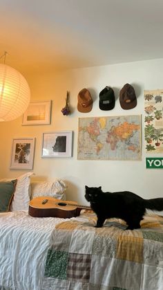 a black cat sitting on top of a bed next to a wall with pictures and hats