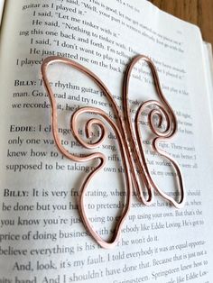 a bookmark made out of copper wire sitting on top of an open page of a book