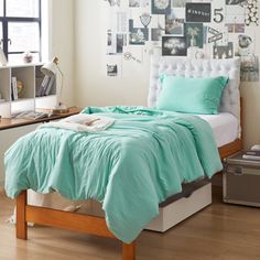 a bed with green sheets and pillows in a bedroom next to a wall with pictures on it