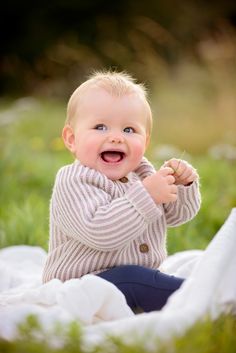 a baby is smiling while sitting in the grass