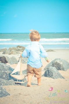 a little boy walking on the beach with a toy boat