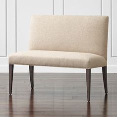 a beige bench sitting on top of a hard wood floor next to a white wall