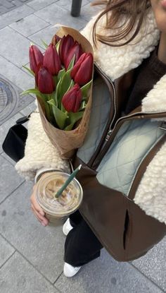 a woman holding a bouquet of red tulips and a drink in her hand