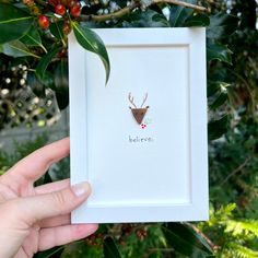 a hand holding up a white frame with a deer's head on it