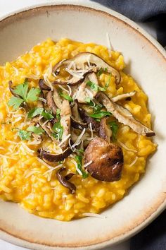 a white bowl filled with yellow riso covered in mushrooms and parmesan cheese