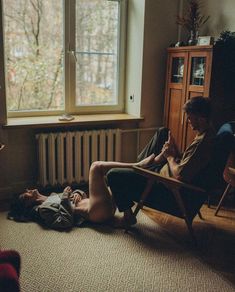 two people are sitting in chairs and one person is laying on the floor near a window