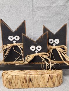 three black cats made out of wood sitting on top of a piece of woven material