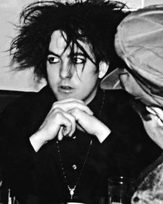 a black and white photo of a man with his hair blowing in the wind while sitting at a table