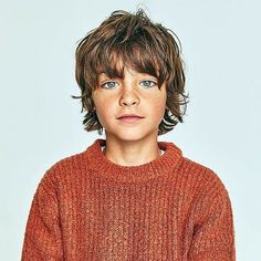 a young boy in an orange sweater is looking at the camera and has his hands on his hips