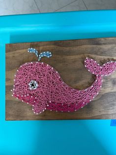 a pink whale string art on a wooden board