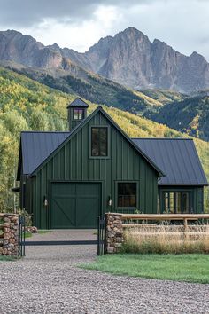 a green barn with mountains in the background and a wooden gate leading to it's entrance