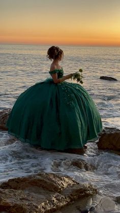 a woman in a green dress is sitting on rocks by the ocean at sunset or sunrise