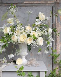 a vase filled with white flowers sitting on top of a table next to greenery