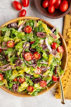 a salad in a bowl with tomatoes and onions on the side, next to a cutting board