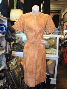 "This is a vintage cotton gingham front button dress in pumpkin and gold, from the 1950's or early 1960's It features short sleeves with ruffles and lace trim, and plastic buttons and matching crochet style lace all the way down the front. The label is from \"Modern Classics\". The belt is here, and the original hang tag. This dress is in excellent shape, clean and ready to wear! Comes from a smoke free home. Measurements: Bust: 40\" Waist: 28\" Hip: 42\" Across Shoulder: 15\" Sleeve Length: 9\" Retro Gingham Vintage Dress, Vintage Fitted Plaid Dress For Picnic, Fitted Vintage Plaid Dress For Picnic, Retro Short Sleeve Plaid Gingham Dress, Vintage Gingham Dress With Short Sleeves, Plaid Vintage Summer Dress, Summer Plaid Vintage Dress, Vintage Fitted Plaid Cotton Dress, Fitted Vintage Cotton Plaid Dress