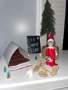 an elf is sitting on a chair next to some rocks and a sign that says elf camp site