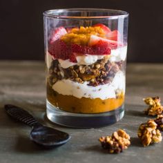 a dessert with strawberries, granola and yogurt in a glass next to a spoon