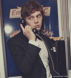 a young man in a suit talking on a phone while standing next to a wall