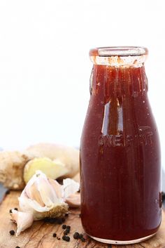 a jar filled with ketchup sitting on top of a wooden cutting board next to garlic