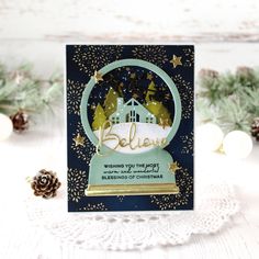 a handmade christmas card with a snow globe on it and pine cones in the background