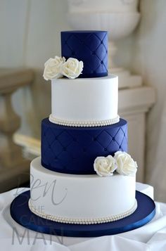 a three tiered wedding cake with white flowers on the top and navy blue bottom