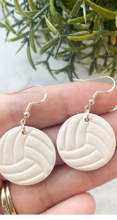 a pair of white earrings sitting on top of a palm tree next to a potted plant