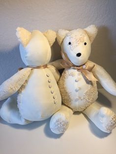 two white teddy bears sitting next to each other on top of a table with a wall in the background