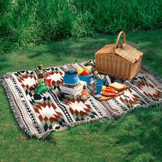 a picnic blanket with food on it in the grass next to a basket and teapot