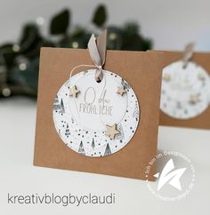 two christmas tags on brown paper with white and silver stars hanging from the tag, one for each ornament