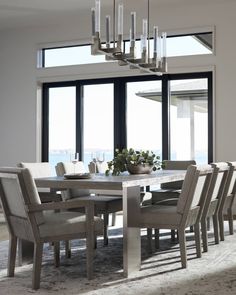 a dining room table with chairs and a chandelier in front of large windows