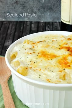 a white bowl filled with macaroni and cheese next to a bottle of wine