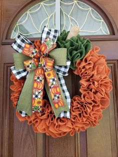 an orange and green wreath on the front door is decorated with pumpkins, ruffles and leaves