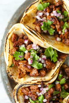 three tacos filled with meat, onions and cilantro on top of a plate