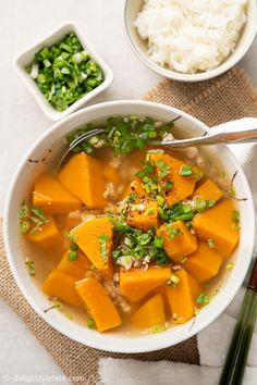 a white bowl filled with soup next to rice and chopsticks