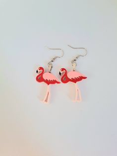 two pink flamingos standing next to each other on a white surface with silver ear wires